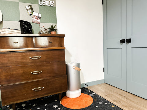 A sleek, gray metal Molekule Air Purifier sits next to a wood dresser in a beautiful home